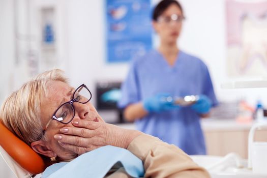 Elderly patient in pain at dentist clinic waiting diagnosis from doctor in medical office. Senior woman in healthcare hospital accusing and complaining about tooth.