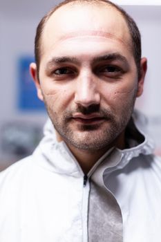 Close up of exhausted pediatric dentist man marks on face because of protection mask. Portrait of tired stomatologist wearing coronavirus ppe suit looking at camera.