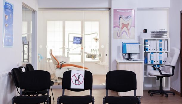 Waiting room in clinic with nobody in it, front office with new normal having sign on chair for social distance in coronavirus pandemic. Empty stomatology reception during covid-19 epidemic.