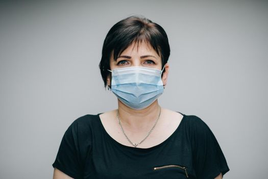 Woman in Medical Mask. Breathes deeply and looking at camera on grey background outdoor. Health care and medical concept