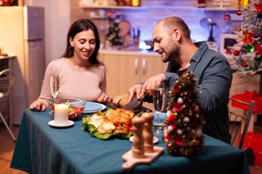 Happy family sitting at dining table in xmas decorated kitchen celebrating christmas holiday. Romantic cheerful couple eating xmas dinner enjoying spending winter season together