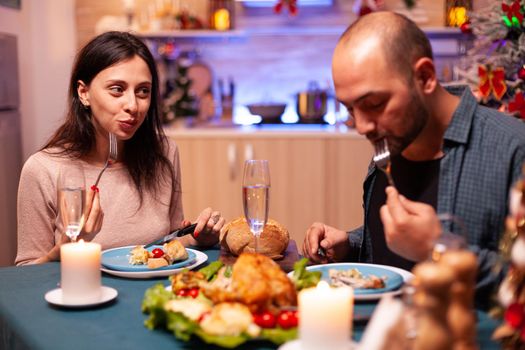 Happy family celebrating christmas holiday enjoying spending winter season together sitting at dining table in xmas decorated kitchen. Cheerful couple eating delicious x-mas dinner