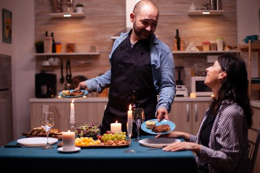 Husband serving wife with tasty food during celebration of relationship in kitchen. Man preparing festive dinner with healthy food, cooking for his woman a romantic dinner,