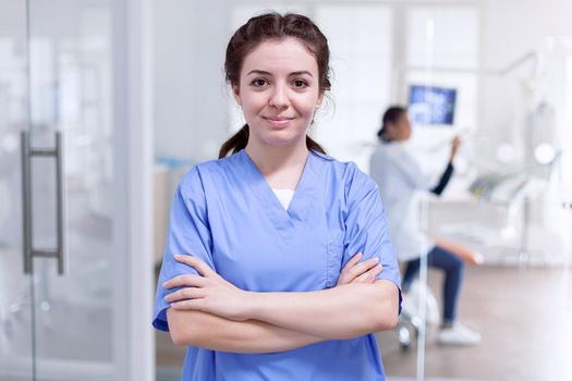 Portrait of stomatology nurse in dental reception with arms crossed looking at camera wearing uniform. Happy smiling assistant in orthodontic office.