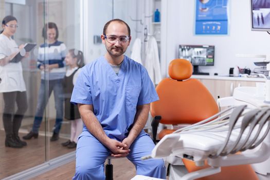 Professional dentist wearing protection and patient discussing with orthodontist. glasses Stomatolog in professioanl teeth clinic smiling wearing uniform looking at camera.