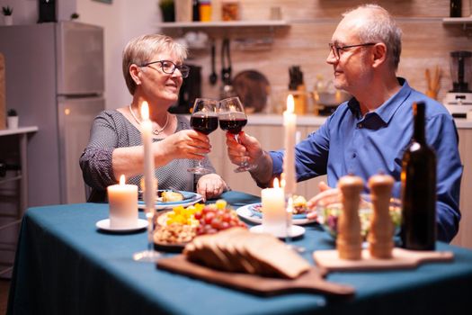 Elderly celebrating marriage with festive dinner in kitchen. Happy cheerful senior elderly couple dining together in the cozy kitchen, enjoying the meal, celebrating their anniversary.