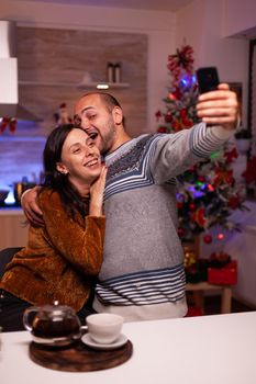 Smiling family taking selfie using smartphone enjoying christmas time standing in xmas kitchen. Happy joyful family celebrating winter holiday season. New year festive season