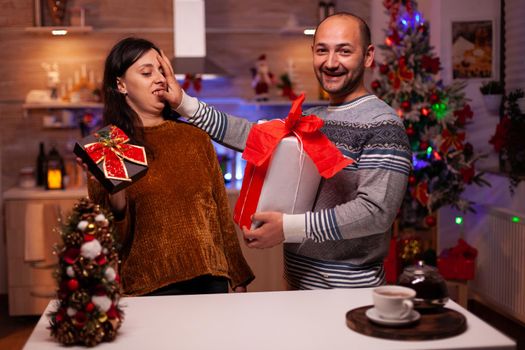 Happy family enjoying spending time together during christmas holiday holding xmas decorated present gift with ribbon on it. Excited married couple celebrating winter festive season