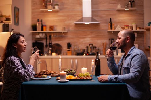 Couple enjoying a glass of wine. Relax happy people clinking, sitting at table in kitchen, enjoying the meal, celebrating anniversary in the dining room.