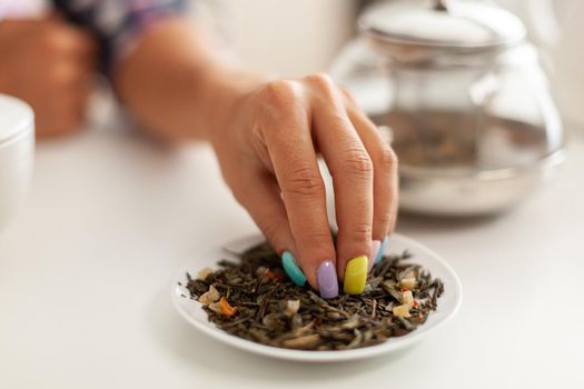 Woman preparing green tea using armoatic herb in kitchen for breakfast. Preparing tea in the morning, in a modern kitchen sitting near the table. Putting with hands, healthy herbal in pot.