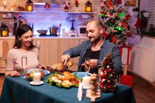 Happy romantic couple eating christmas dinner sitting at dinning table in xmas decorated kitchen. Cheerful family celebrating christmastime enjoying spending winter holiday together