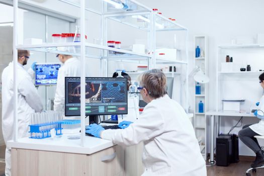 Doctor in chemistry and her multiethnic teamn engineering drug. Senior scientist in pharmaceuticals laboratory doing genetic research wearing lab coat with team in the background.