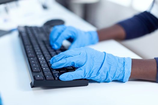 Close up of african researcher holding hands on computer keyboard Black healthcare scientist in biochemistry laboratory wearing sterile equipment.