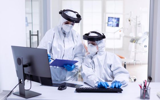 Dentist and nurse during global outbreak in protective suit against infection with covid-19. Medicine team wearing protection gear against coronavirus pandemic in dental reception as safety precaution.