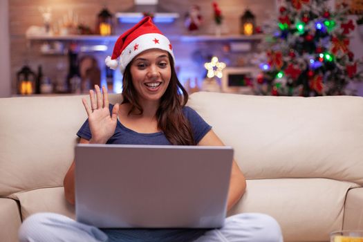 Smiling woman greeting remote friends enjoying christmastime together during online videocall meeting conference using laptop computer. Adult person celebrating christmas holiday season