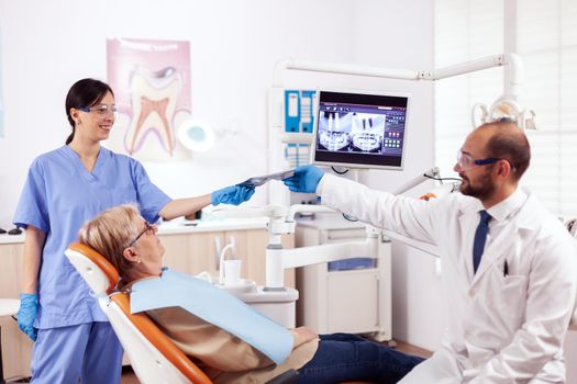 Dentist assistant giving doctor radiography of senior woman waiting. Medical teeth care taker holding patient radiography sitting on chair during consultation.