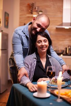 Romantic couple looking at webcam during romantic dining. Married people special tender moments, enjoying the meal at candle lights celebration.