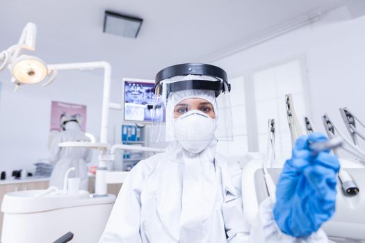 Patient pov of dentist in covid suit examining mouth hygine using dental tools. Stomatolog wearing safety gear against coronavirus during heatlhcare check of patient.