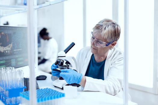 Senior scientist putting glass slide on microscope during medical investigation. Elderly researcher carrying out scientific research in a sterile lab using a modern technology.