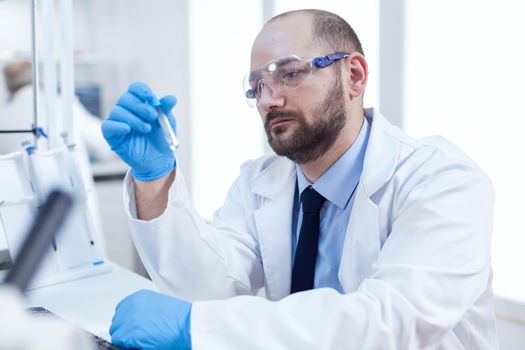 Genetic scientist conducting pharmacology exepriment, Researcher in biotechnology sterile lab holding analysis in tube wearing gloves and protection glasses.