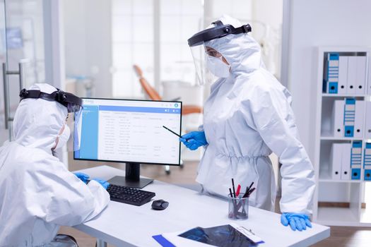 Dentist doctor wearing ppe suit talking with nurse at reception about patients schedule. Medicine team wearing protection gear against coronavirus pandemic in dental reception as safety precaution.