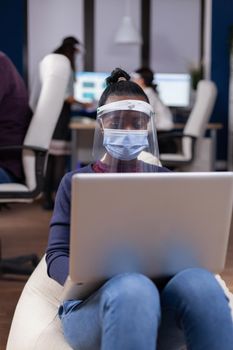 African manager in comany using laptop wearing face mask against covid. Multiethnic business team working respecting social distance during global pandemic with coronavirus.