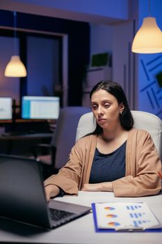 Skilled businesswoman working on computer connected to wireless internet finishing a deadling. Smart woman sitting at her workplace in the course of late night hours doing her job.