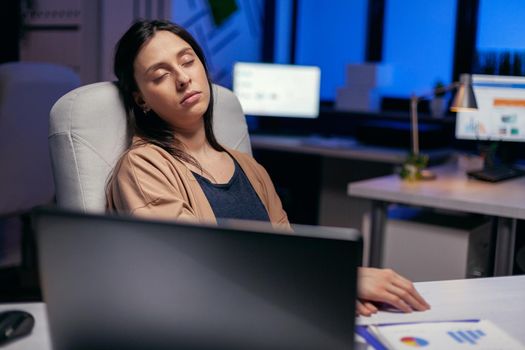 Stressed tired businesswoman sleeping in empty office in the course of working overtime. Employee falling asleep while working late at night alone in the office for important company project.