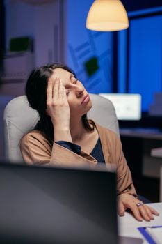 Tired businesswoman keeping eyes closed rubbing forehead because exhausting. Employee falling asleep while working late at night alone in the office for important company project.
