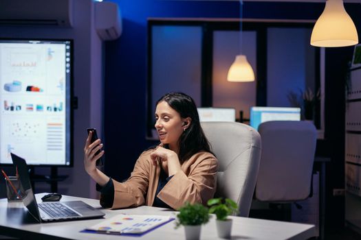 Freelancer talking during virtual meeting at midnight in empty working place. Woman working on finance during a video conference with coworkers at night hours in the office.