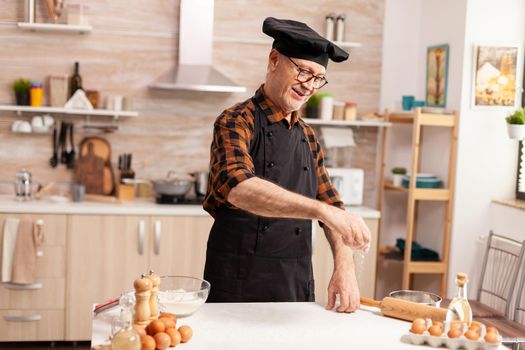 Retired chef in home kitchen spreading wheat flour over table while preparing handmade Cook f with bonete and apron, in kitchen uniform sprinkling sieving sifting ingredients by hand.