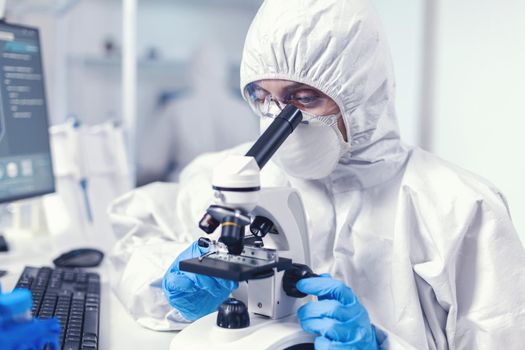 Woman scientist in laboratoruy searching for coronavirus cure dressed in ppe suit. Chemist researcher during global pandemic with covid-19 checking sample in biochemistry lab