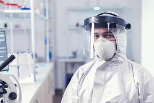 Fatigued medical scientist sitting at workplace wearing coverall with face mask against covid19 . Overworked researcher dressed in protective suit against invection with coronavirus during global epidemic.