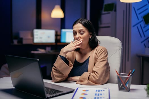 Exhausted businesswoman yawning working on important project in financial firm. Smart woman sitting at her workplace in the course of late night hours doing her job.