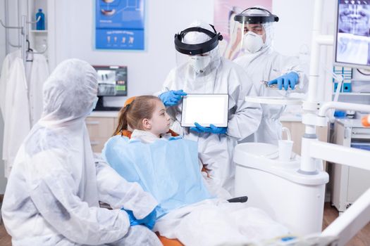 Dentist dressed in ppe suit using digital device with chroma key Medical specialist in oral hygine holding tablet pc with copy space available during global pandemic with covid19.