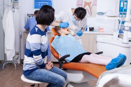 Dentist in the course oral treatment for little kid with caries. Dentistry specialist during child cavity consultation in stomatology office using modern technology.