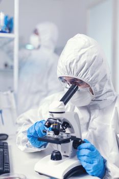 Close up of coronavirus scientist checking vaccine evolution dressed in ppe using microscope. Chemist researcher during global pandemic with covid-19 checking sample in biochemistry lab