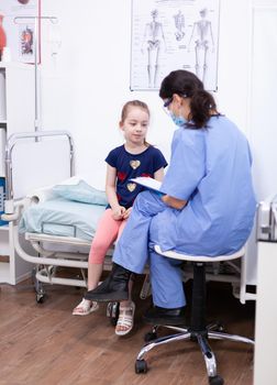 Nurse consulting child laying in bed wearing protection mask during coronavirus. Health doctor specialist providing health care services consultations treatment in protective equipment.