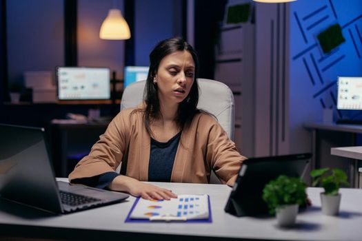 Entrepreneur using tablet pc while working from dark office working on deadline. Business woman working overtime at the office to finish a corporate job using tablet pc.