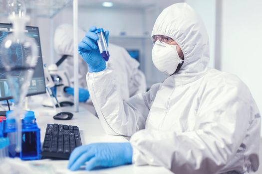 Doctor conducting scientific virus research holding test tube. wearing ppe suit. Scientist in laboratory wearing coverall doing research and analyzing substance during global pandemic with covid19.
