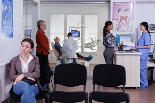 Patients in stomatology reception waiting in line taking filling form, doctor examining senior man discussing teeh healthcare. Stomatology corridor with people waiting consultation.