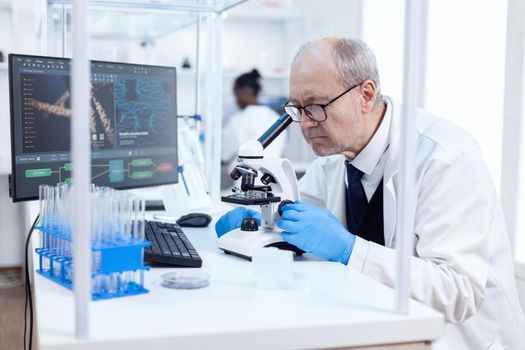 Senior scientist in chemistry laboratory uses microscope working on new medicine. Chemist researcher in sterile lab doing experiments for medical industry using modern technology.