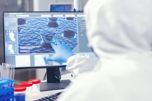Medical researcher analysing evolution of coronavirus pointing at screen in modern facility dressed in . Lab engineers conducting experiment for vaccine development against covid19 virus