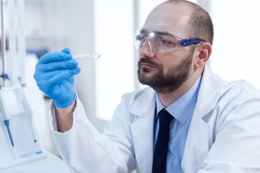 Chemist scientist holds test tube of glass in his hand for medicine experiment. Researcher in biotechnology sterile lab holding analysis in tube wearing gloves and protection glasses.