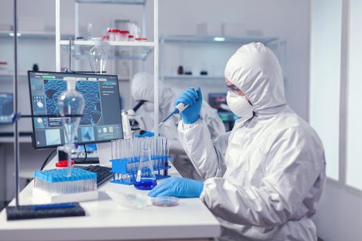 Healthcare scientist taking sample from test tube using automatic pipette in modern lab. Chemist in modern laboratory doing research using dispenser during global epidemic with covid-19.