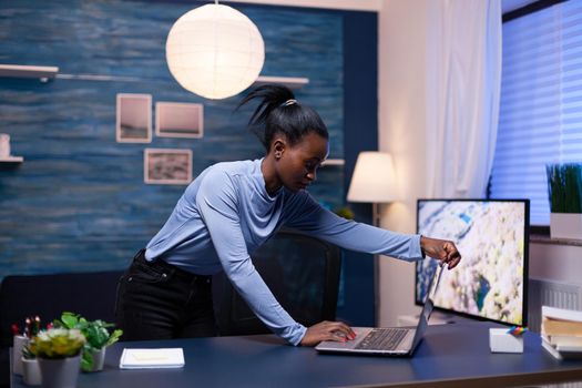 African entrepreneur working from home late at night using laptop to workin on important project. Black entrepreneur sitting in personal workplace writing on keyboard.