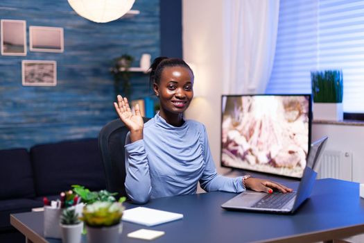 Dark skinned entrepreneur waving in the course of conversation during remote video call. African business woman saying hello Black freelancer working with remotely team chatting virtual online conference.