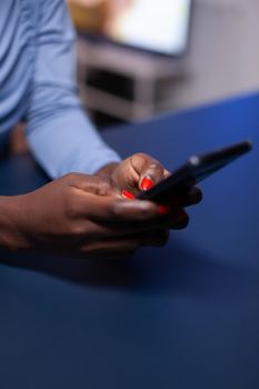 Close up of black woman hands telecommuting late at night from living room sitting at desk. Employee using modern technology network wireless doing overtime.