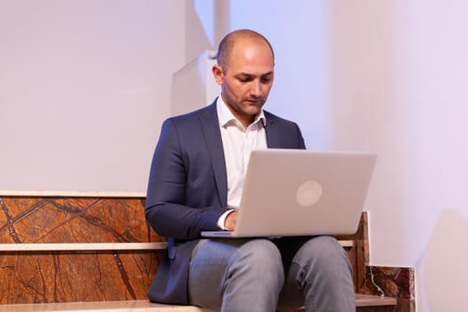 Stressed exahusted businessman working on business deadline using laptop. Confident corporate entrepreneur using laptop doing overtime sitting on stairwell.