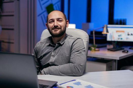 Confident entrepreneur looking confident looking at camera in empy office. Smart businessman sitting at his workplace in the course of late night hours doing his job.